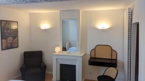 A room with a fireplace, a mirror, two wall-mounted lights, a chair, and a shelf.