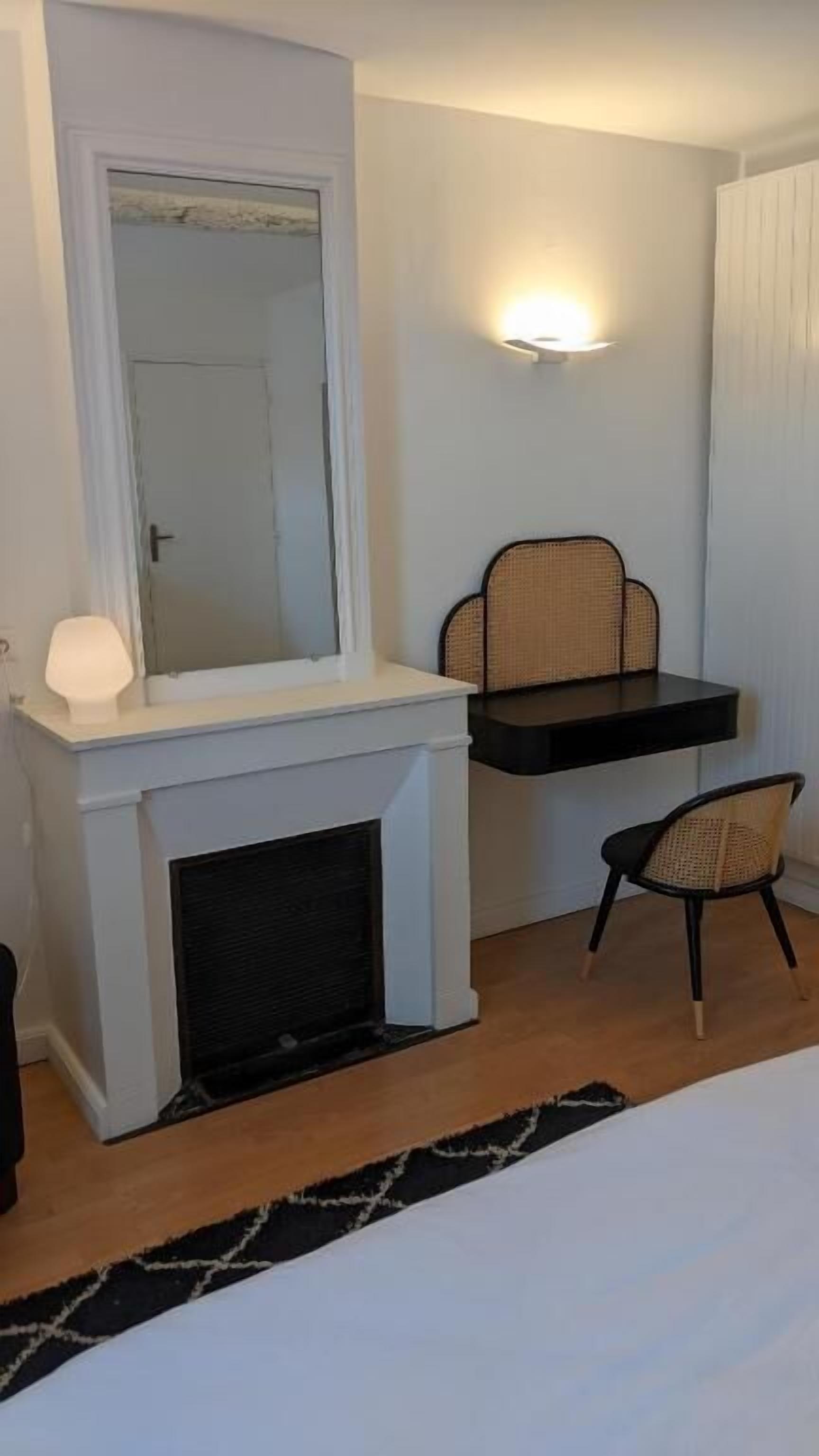 A bedroom with a fireplace, a mirror, a wall-mounted shelf, a chair, and a bed.