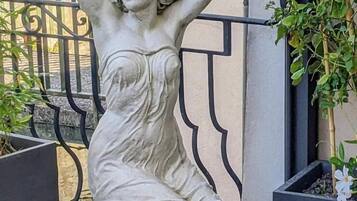 Una estatua de una mujer con vestido, ubicada junto a una reja metálica y plantas en macetas.