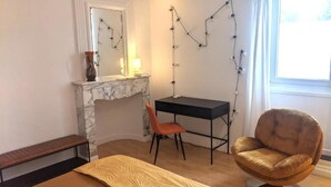 A room with a marble fireplace, a desk, a chair, a bed, and a window with curtains.