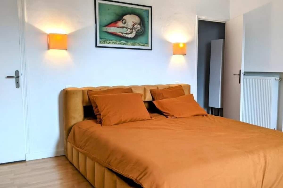 Un dormitorio con cama, dos luces fijadas a la pared, un radiador y un cuadro enmarcado.