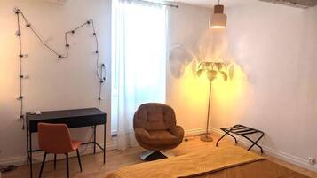 Une pièce comprenant un bureau, une chaise, un lit, une lampe sur pied et une fenêtre avec des rideaux.