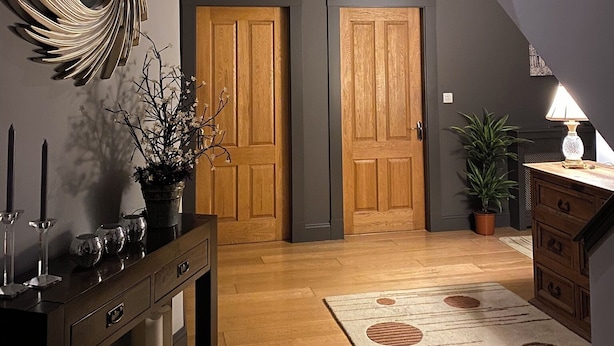 Una scala con una parete scura e un soffitto luminoso, una porta in legno, un tavolo consolle con uno specchio, una pianta in vaso e una lampada.