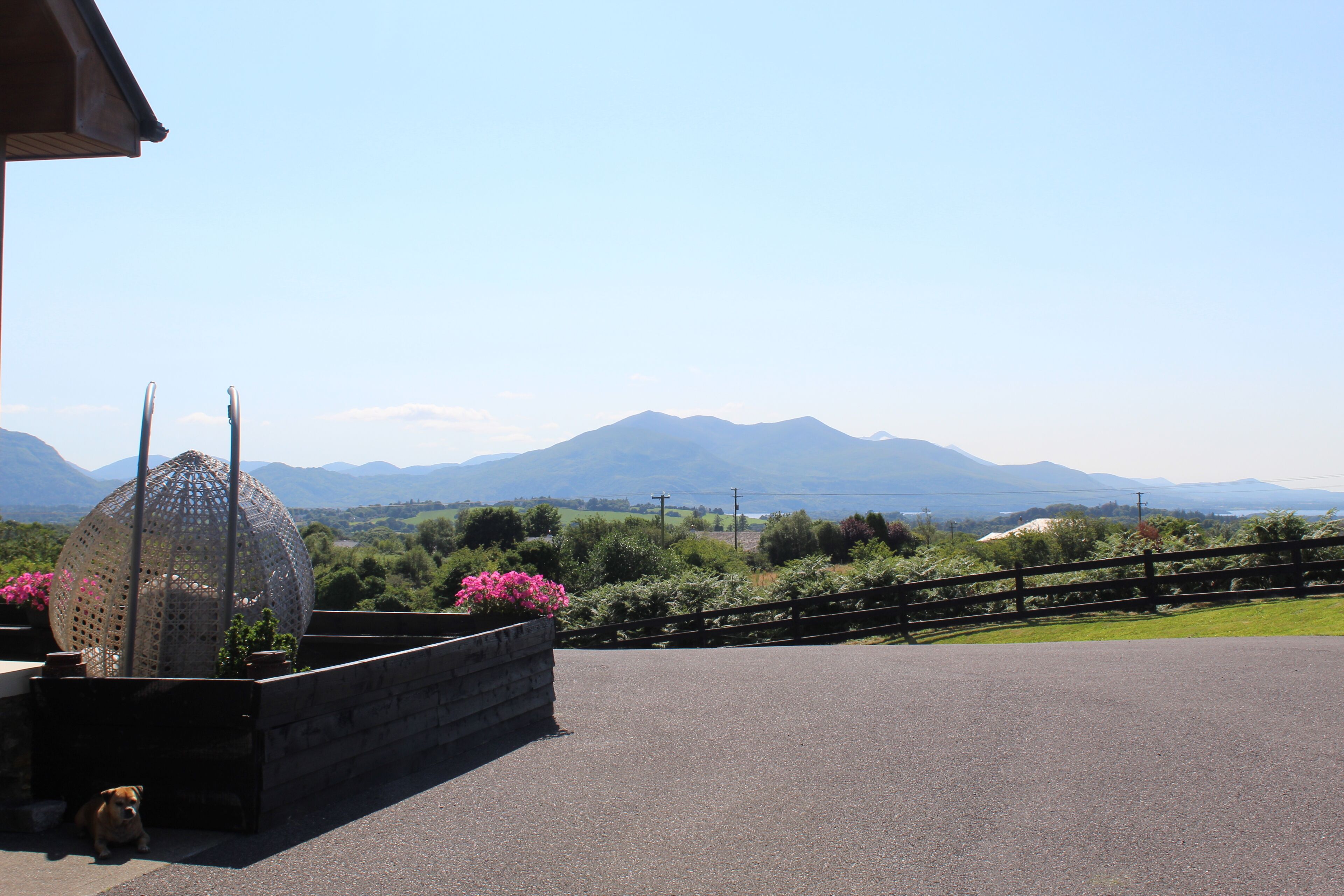 A paved area with a stone planter, a wooden fence, and a view of distant mountains.