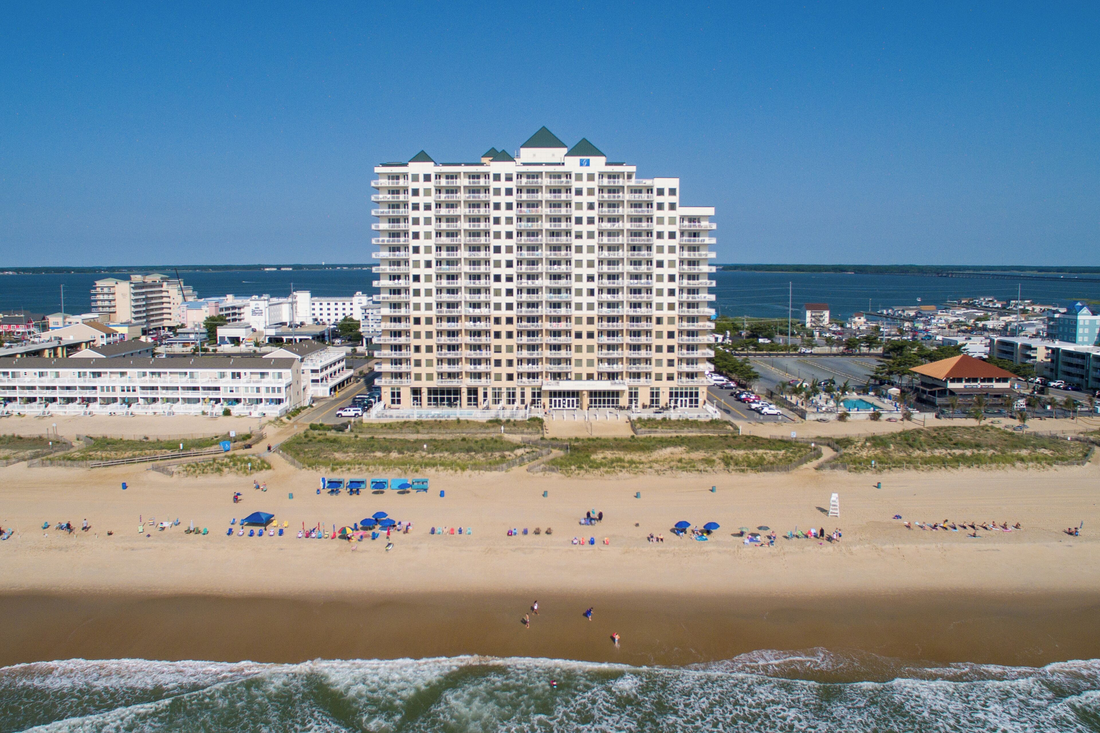 A beachfront hotel with multiple floors, a sandy beach in front, and a view of the ocean.