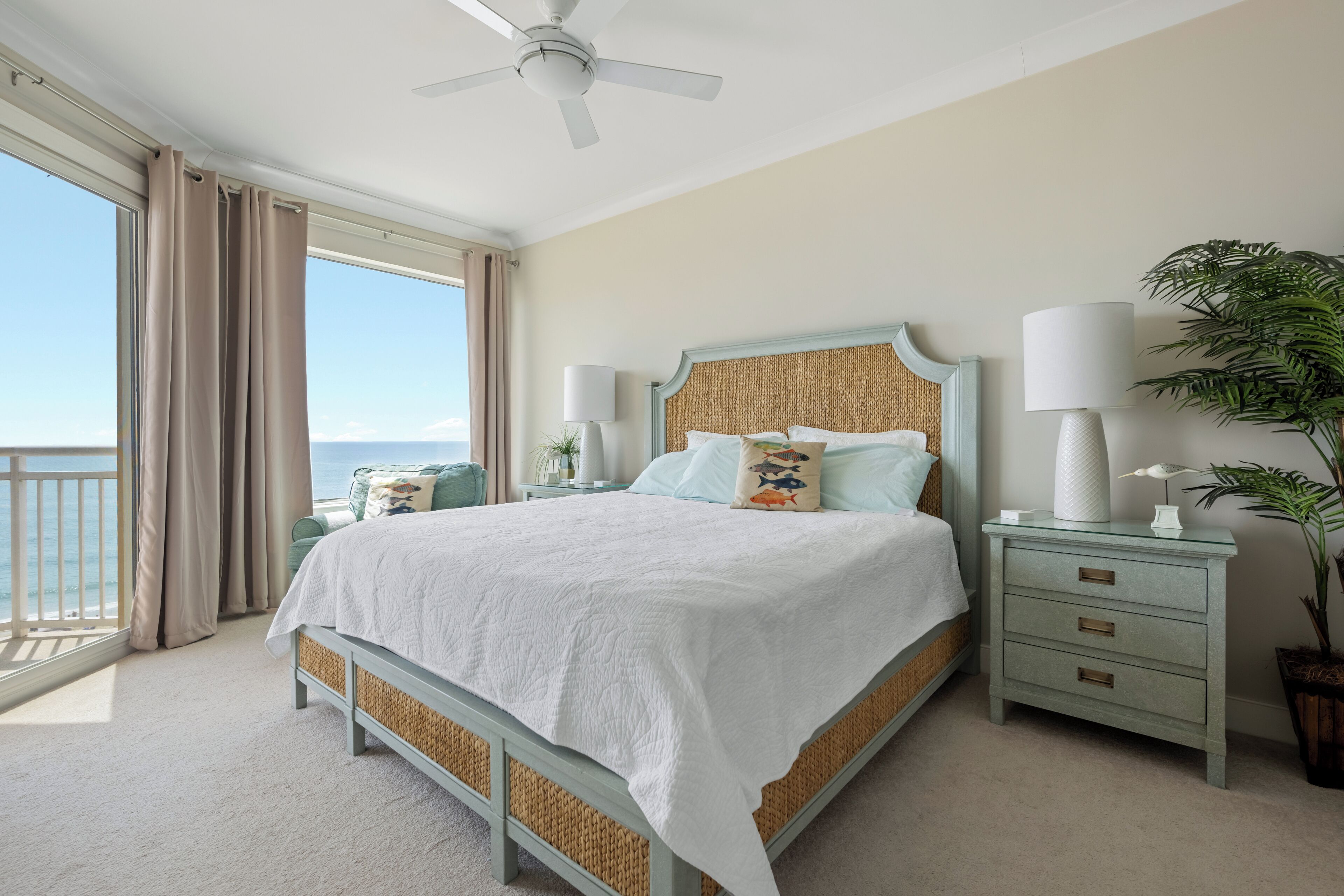 Een slaapkamer met een bed, nachtkastjes, een plafondventilator en uitzicht op de oceaan.