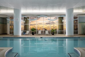 Ein Innenpool mit großen Glaswänden, Blick auf den Sonnenuntergang und Liegestühlen mit Pflanzgefäßen.