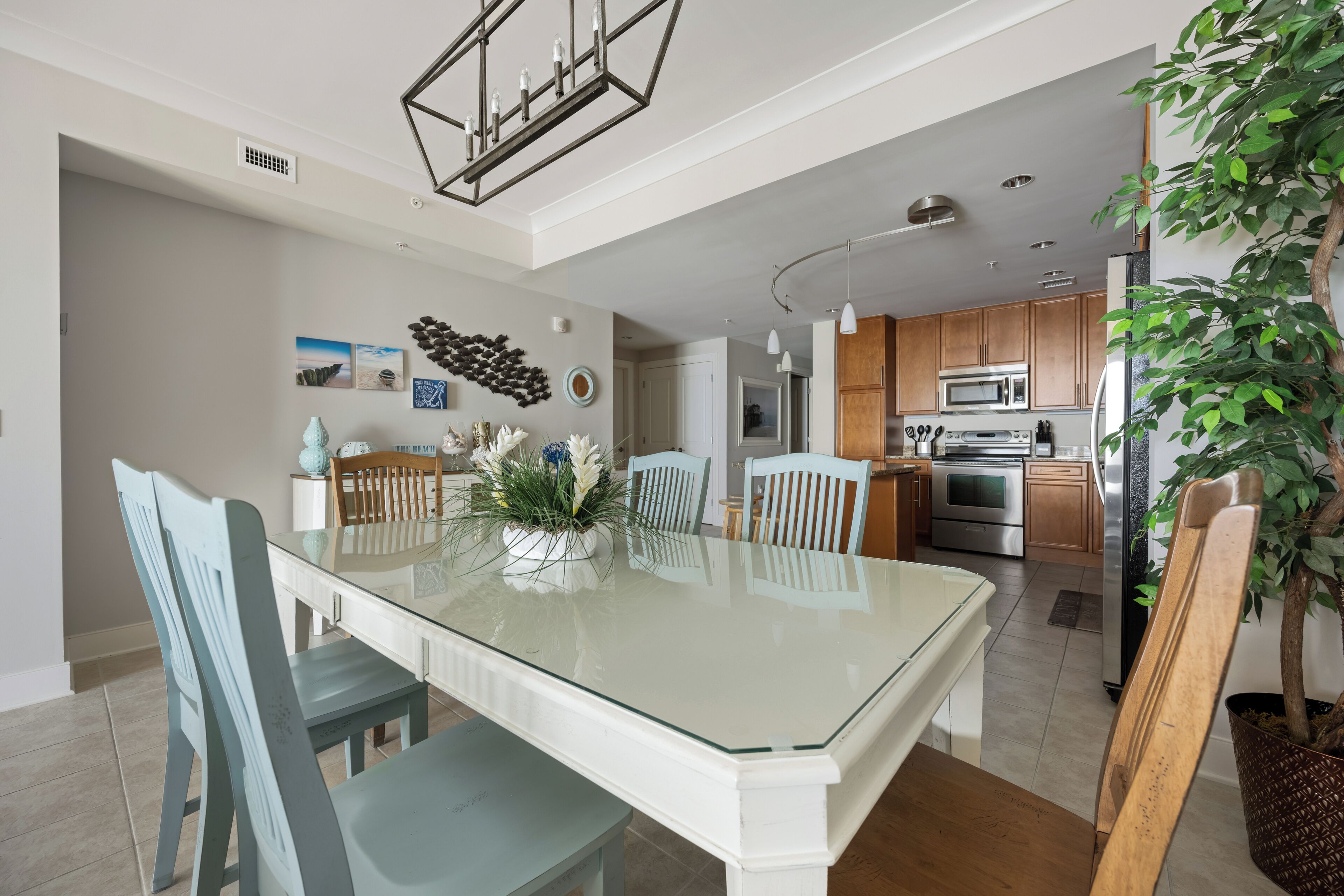 Una cocina moderna con electrodomésticos de acero inoxidable, una zona de comedor con una mesa y sillas de superficie de vidrio, y una planta grande en maceta.