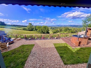 Un patio con un jacuzzi, una parrilla y una terraza de madera con vistas a un paisaje pintoresco.