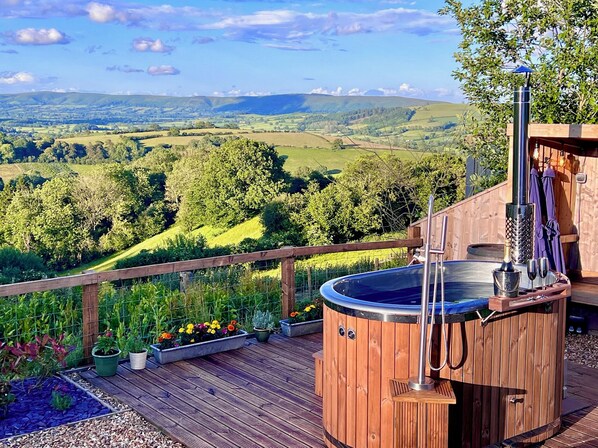 A hot tub on a wooden deck with a scenic view of rolling hills and a wooden fence. - Olive Hut (Bishops Castle)