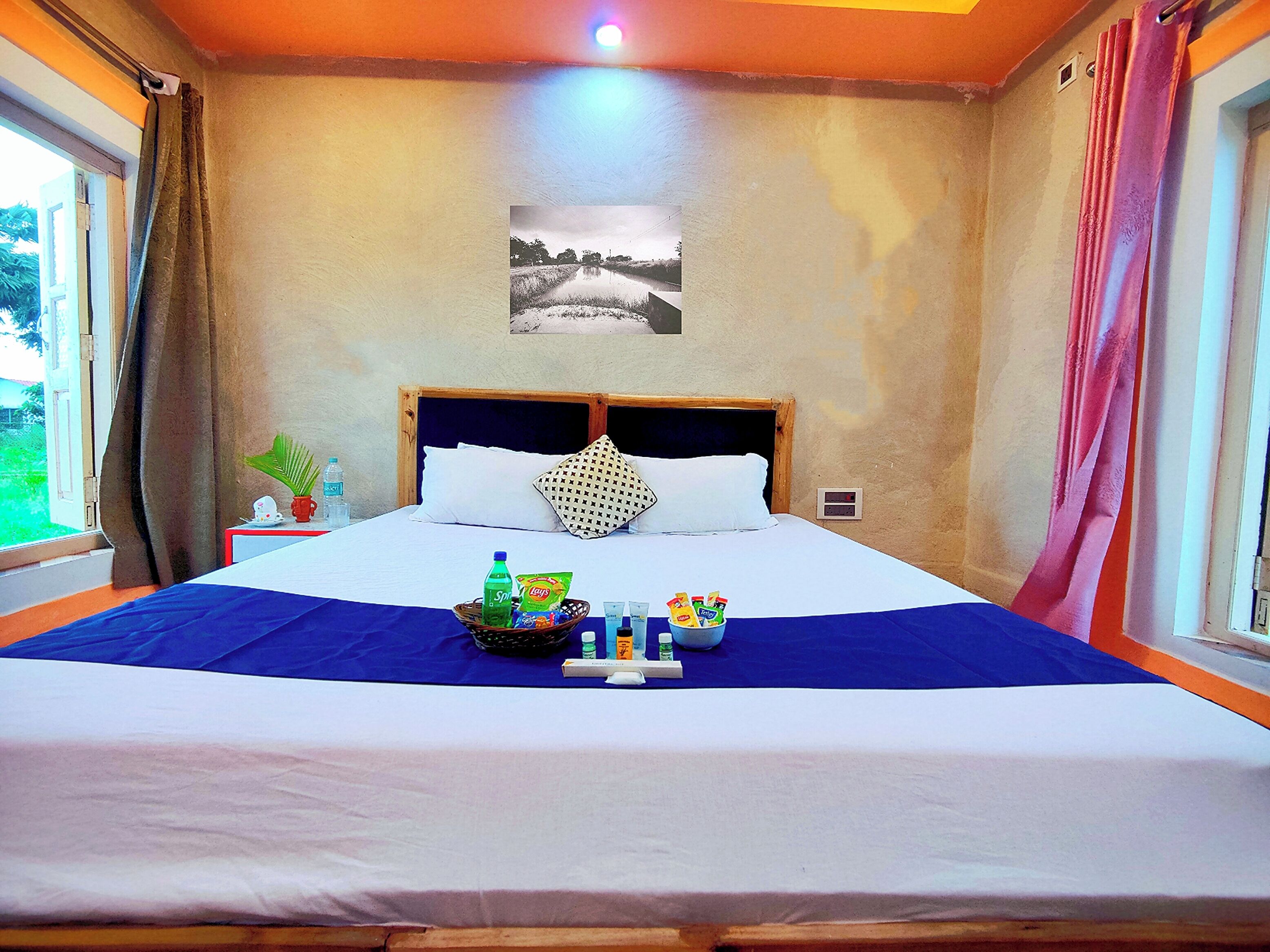 A hotel room with a large bed, a headboard, a bedside table with a plant, a wall clock, and a window with curtains.
