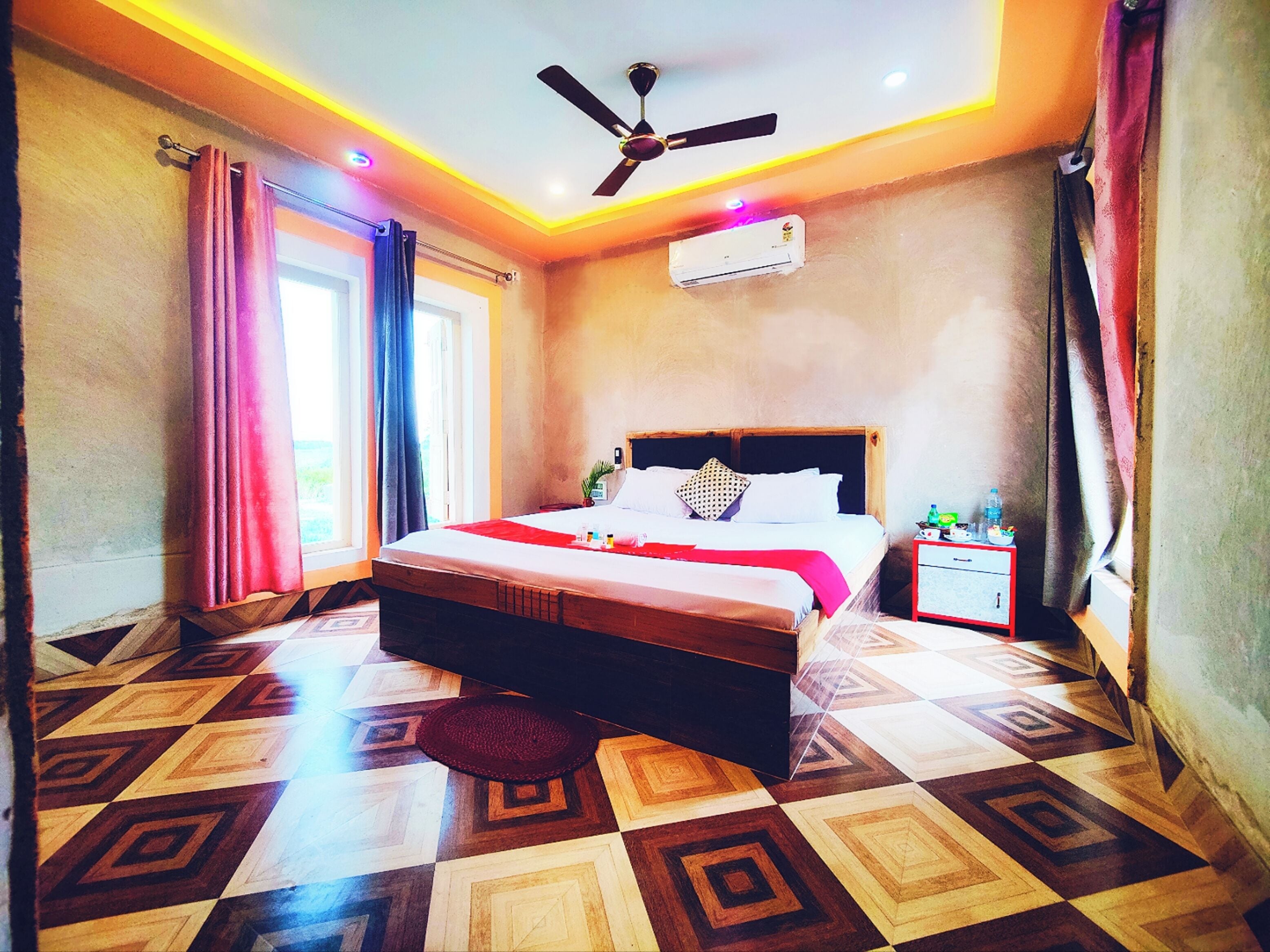 A hotel room with a bed, a ceiling fan, an air conditioning unit, a bedside table, and a patterned floor.