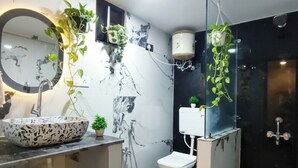 Casa de banho com painel de parede em mármore, espelho redondo, lavatório suspenso, sanita e plantas em vasos.