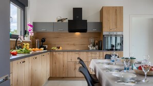 A modern kitchen with wooden cabinets, a black range hood, and a dining area set for a meal. - Villa Bateli by Villas Guide (Barban)