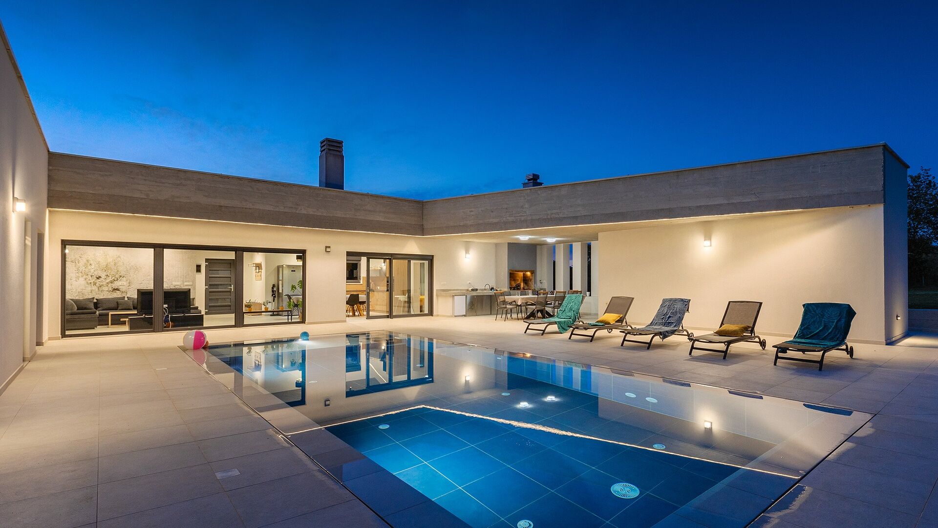 A modern house with a swimming pool, outdoor seating, and a large glass door entrance.