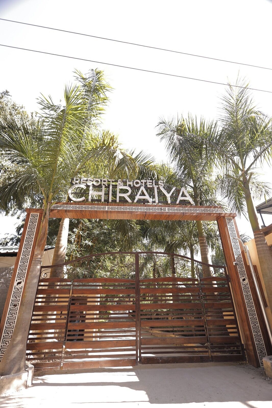 Ein hölzernes Tor mit dem Schild 'CHIRAYA' darüber, umgeben von Palmen.