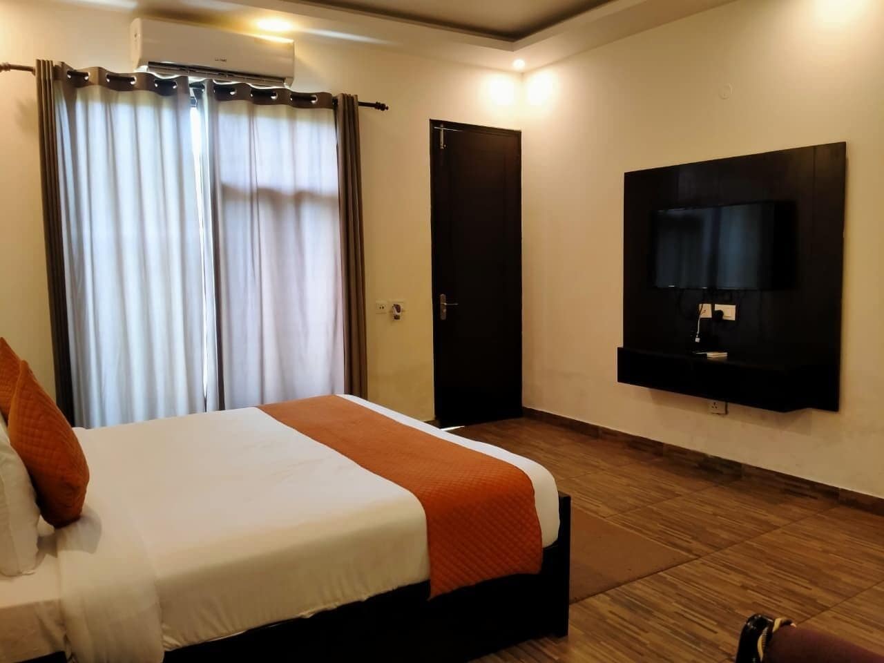 A hotel room with a bed, curtains, a door, and a mounted TV.