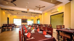 A dining area with multiple tables set for a meal, ceiling fans, recessed lighting, and a large window providing natural light.