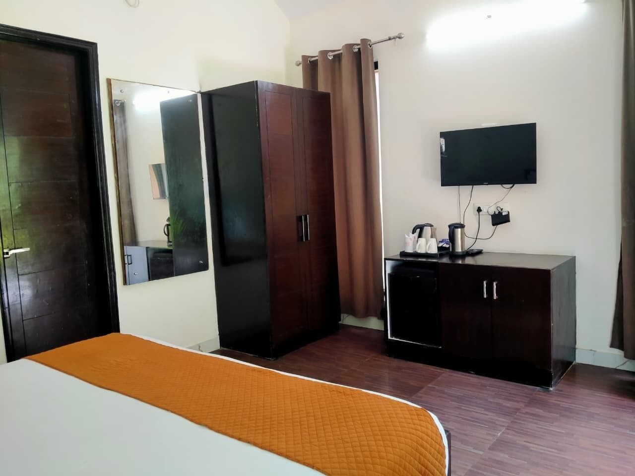 Habitación de hotel con cama, armario, espejo, televisor y un mueble pequeño.