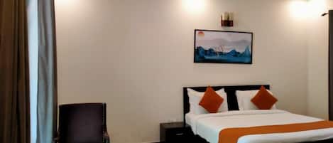 A hotel room with a bed, a chair, a nightstand, and a painting on the wall.