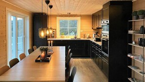 Uma cozinha moderna com mesa de jantar de madeira, armários pretos e luminárias pendentes.