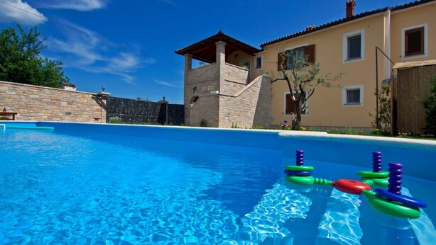 Una piscina con acqua cristallina, circondata da mura in pietra e un edificio con tetto in tegole.