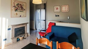 A living room with a fireplace, a blue sofa, a red chair, and a wooden dining table. - Casa Chiara (Picenze di Barisciano)