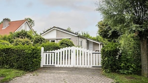 Ein Wohnhaus mit weißem Zierzaun, einem gepflasterten Einfahrt und einem roten Ziegeldach.