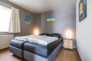 A bedroom with a double bed, two bedside tables, a radiator, and two paintings on the wall. - Coastal Bungalow Stay in Vlissingen (Vlissingen)