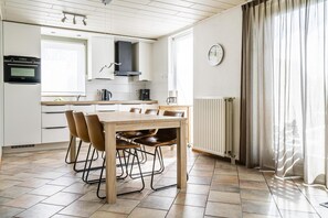 A modern kitchen with a dining table, chairs, a clock, and a window with curtains. - Coastal Bungalow Stay in Vlissingen (Vlissingen)