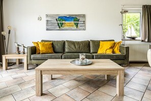 A living room with a green sofa, wooden coffee table, and a painting on the wall. - Coastal Bungalow Stay in Vlissingen (Vlissingen)