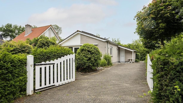 Ein Wohnhaus mit gepflasterter Auffahrt, weißem Zaun und üppiger Bepflanzung.