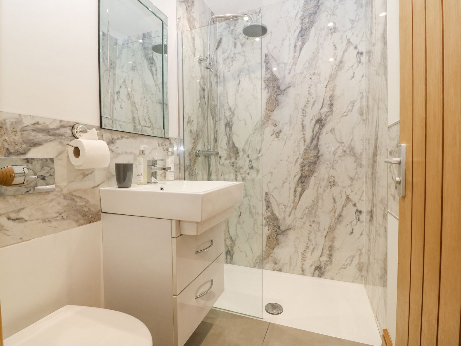 A modern bathroom with a marble shower wall, a white sink, and a toilet.