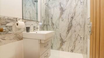A modern bathroom with a marble shower wall, a white sink, and a toilet.