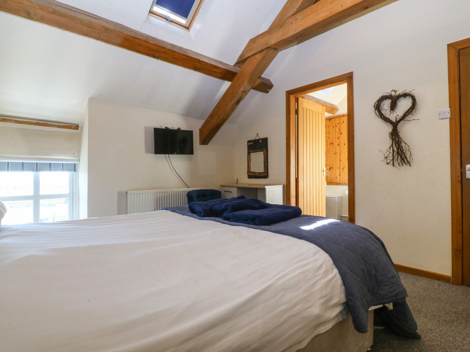 A bedroom with a bed, a television, a mirror, and a heart-shaped decoration on the wall.