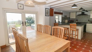 Een eethoek met een houten tafel en stoelen, een keuken met fornuis en spoelbak, en uitzicht door een glazen deur op een terras.