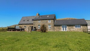 Een stenen huis met een donker dak, een kleine tuin en een heldere blauwe lucht.