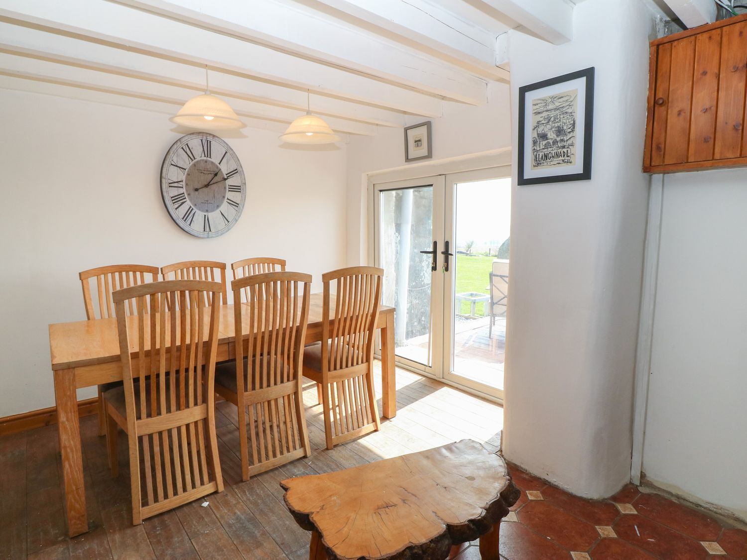 A dining area with a wooden table and chairs, a wall clock, and a door leading outside.