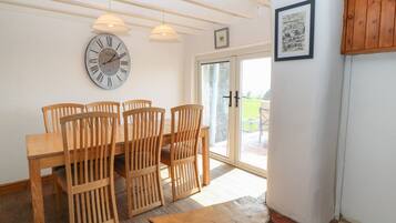 A dining area with a wooden table and chairs, a wall clock, and a door leading outside.