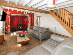 A cozy living room with a fireplace, a grey sofa, a wooden coffee table, and a staircase. - Cefnbron (Caernarfon)