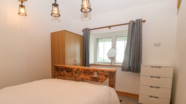 Een slaapkamer met een bed, een houten hoofdbord, een dressoir, een spiegel en een raam met gordijnen.