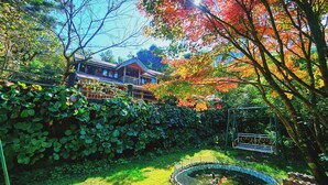 Uma casa japonesa tradicional cercada por vegetação exuberante e um pequeno lago.
