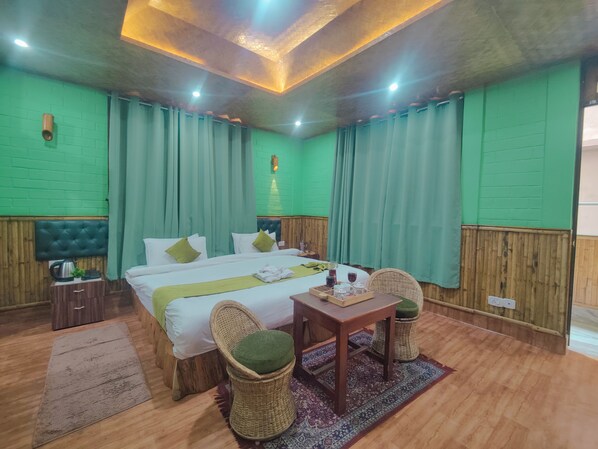 A hotel room with a bed, a table with glasses and a tray, wicker chairs, a green wall, and a wooden floor. - Jo'stel Hotel Bamboo Inn (Gangtok)