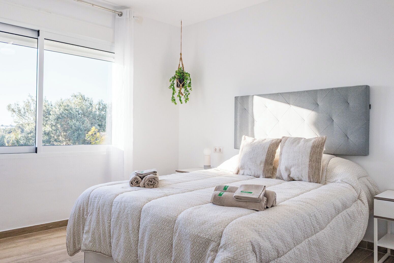 Ein modernes Schlafzimmer mit einem großen Bett, einer hängenden Pflanze und Blick auf Bäume.