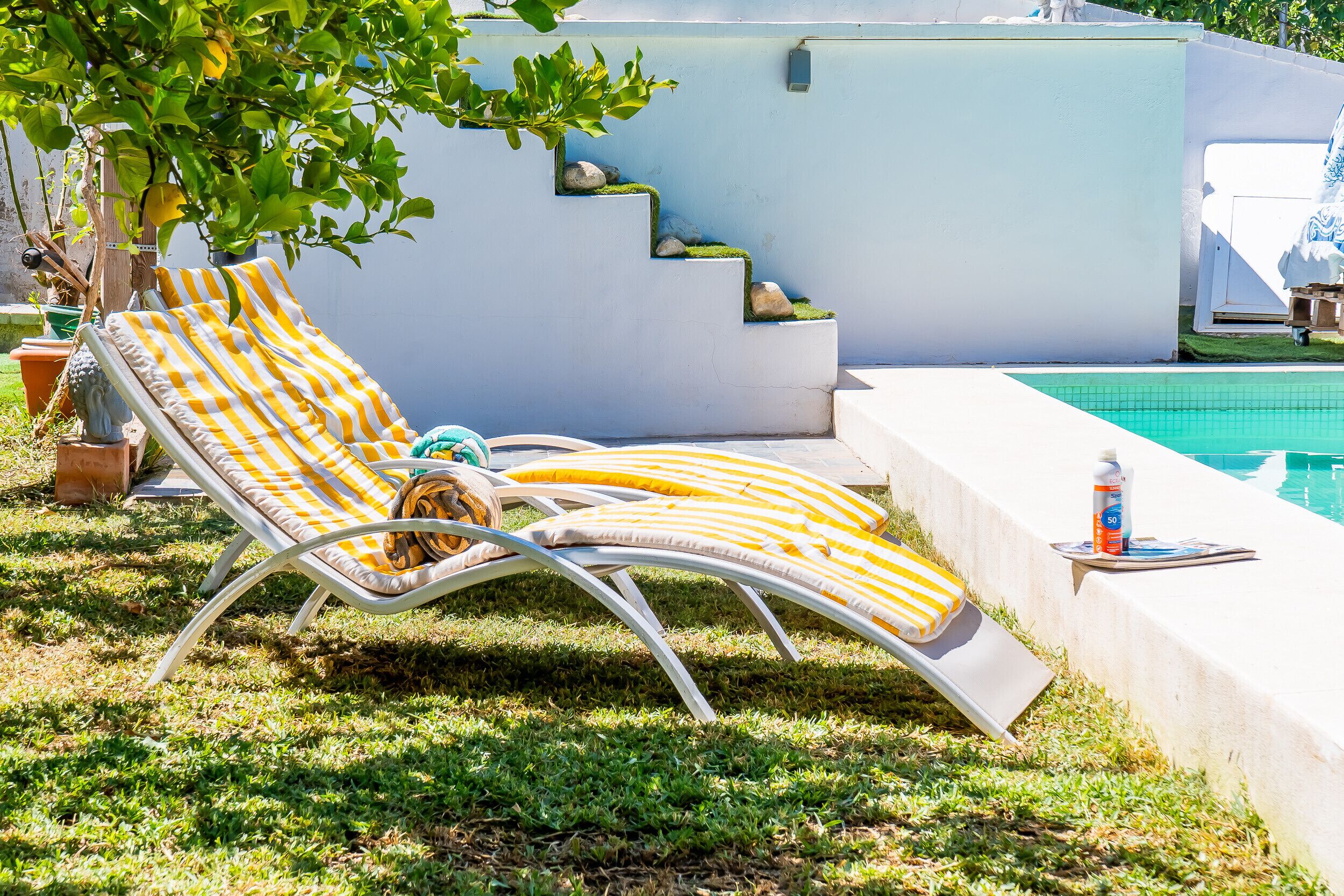Un espace aménagé au bord de la piscine, comprenant deux chaises longues, un petit escalier et la piscine elle-même.