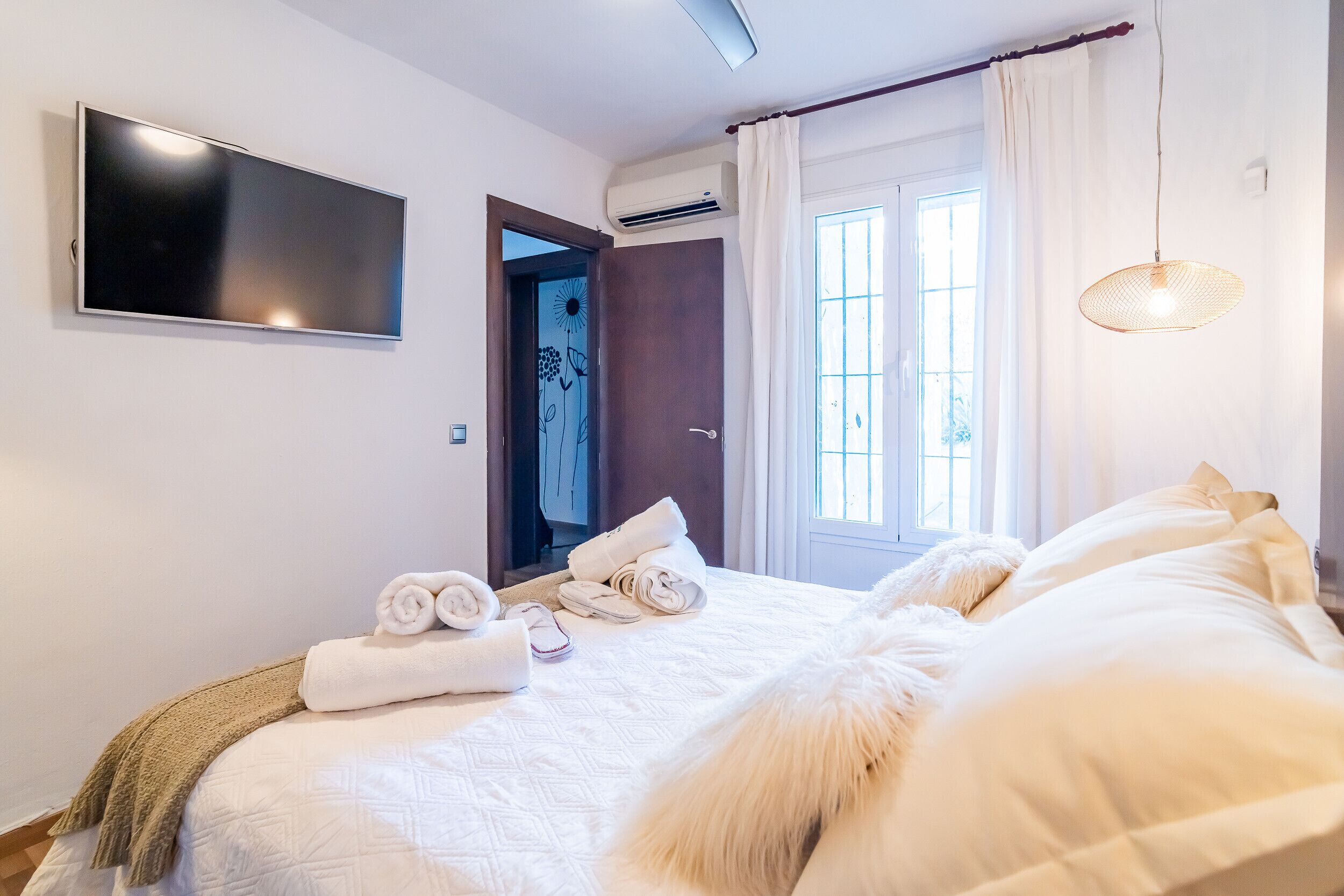 Habitación de hotel con cama, televisión de pantalla plana, ventana con cortinas y aire acondicionado instalado en la pared.