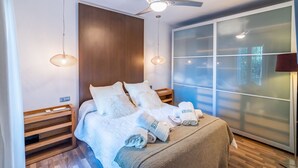 Ein modernes Hotelzimmer mit Bett, Deckenventilator, Nachttischlampen, einem Holznachttisch und einem großen Fenster mit Milchglas.