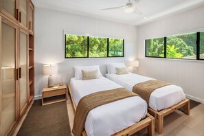 Hotelkamer met twee bedden, een nachtkastje, een lamp, een houten garderobe en grote ramen met uitzicht op groen.