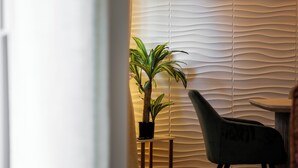 A room with a wooden floor, a small table, a chair, a potted plant, and a wall with a wavy pattern. - Luxury Apartment • 3 Suites • 2 Parking Lots • 5 min Downtown (Strasbourg)