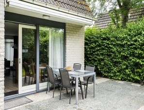 A patio area with a table and chairs, a sliding glass door, and a brick wall. - Home Near Vlissingen Beach (Vlissingen)